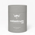 A matte gray cylindrical container for Colostrum Co food capsules, featuring a white logo and text on a clean white background.