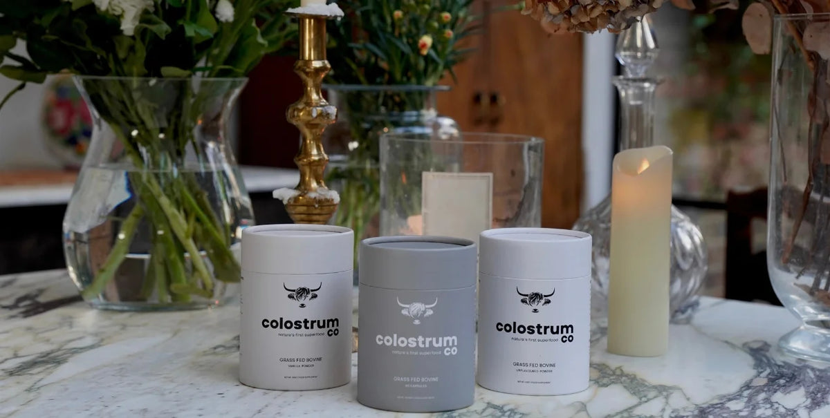 Three containers labeled 'colostrum co' on a marble surface with decorative items in the background.